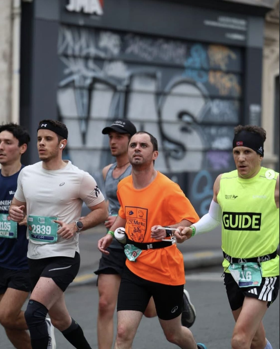 Un coureur A2CMieux accompagné de son guide lors d'une course en ville.