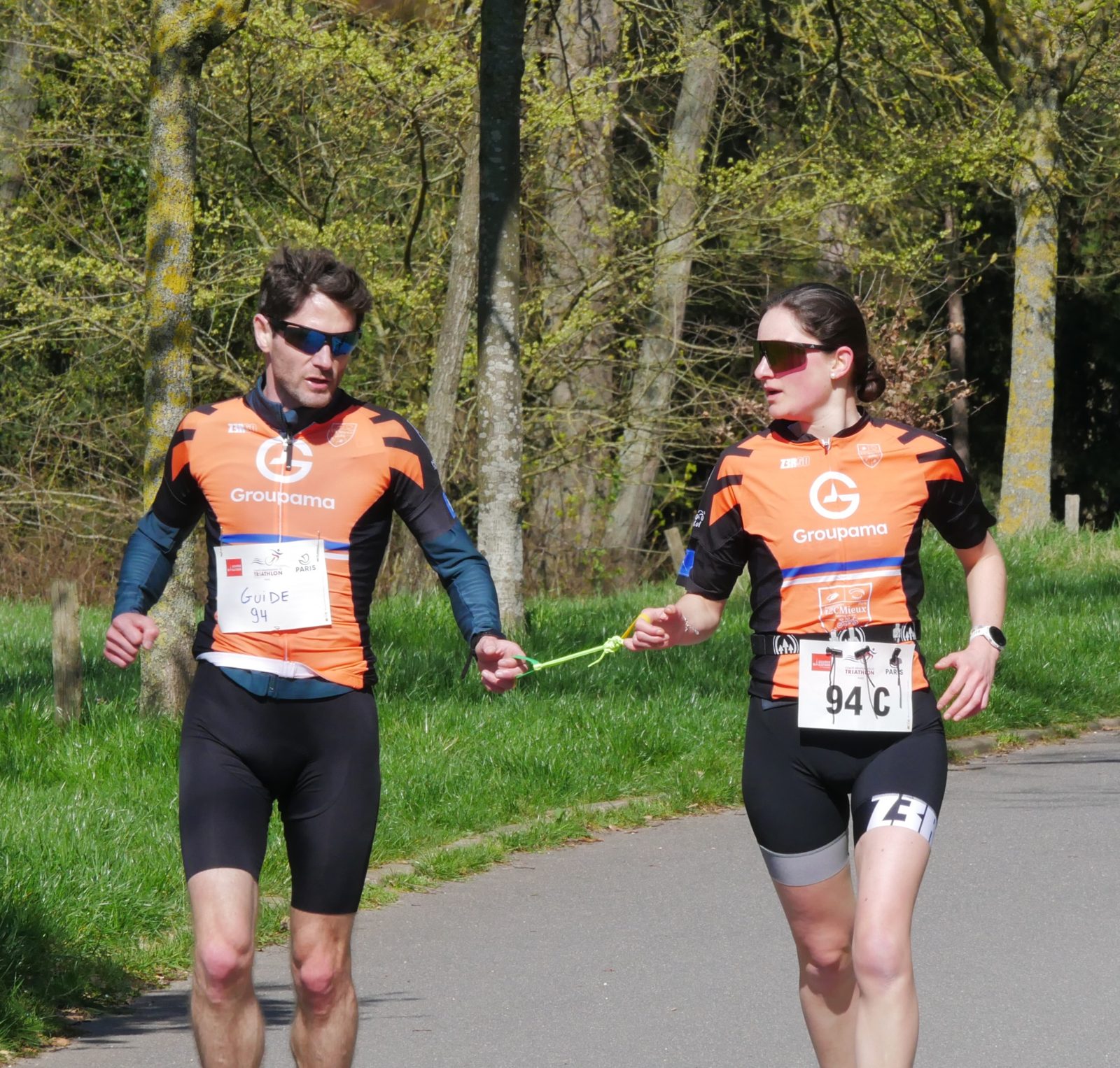 Un guide et une coureuse d'A2CMieux reliés par un cordon de guidage lors d'une course à pied ensoleillée.