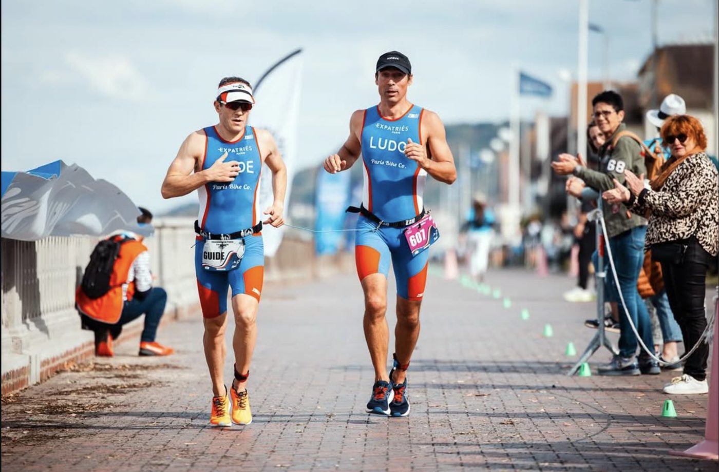 Un duo de coureurs A2CMieux, guide et sportif reliés, lors d'une course urbaine.