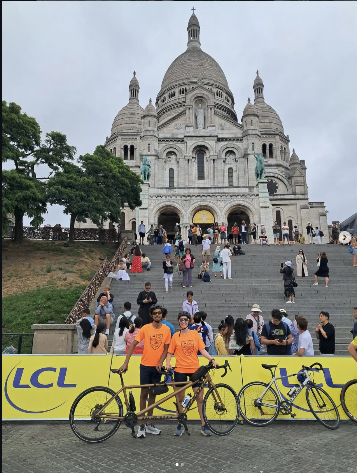 Un duo de cyclistes A2CMieux posant avec leur tandem devant la basilique du Sacré-Cœur à Paris.